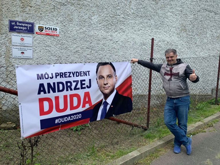 Ksiądz wiesza baner wyborczy Andrzeja Dudy na płocie przy budynku Caritas. „Po pracy” już może?