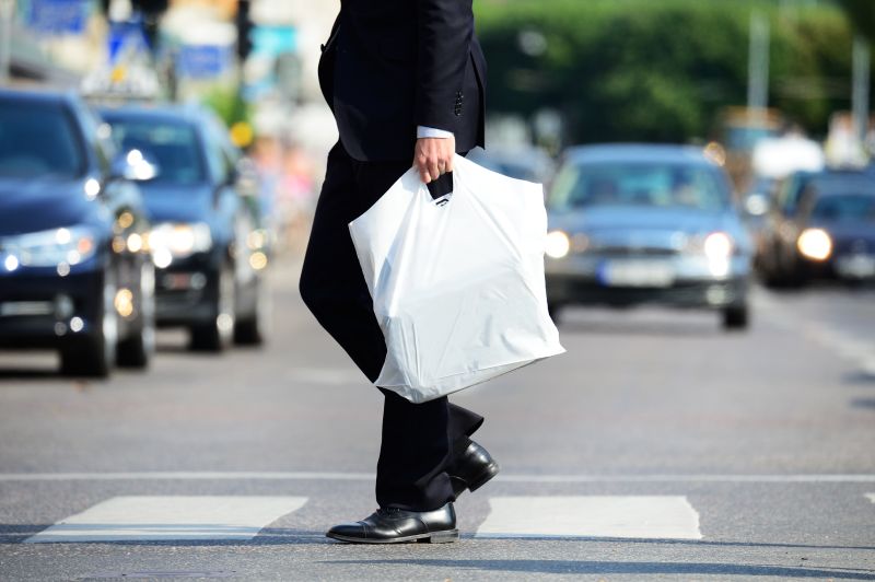 Mężczyzna w garniturze przechodzący przez ulicę z białą plastikową reklamówką - niupak.eu 